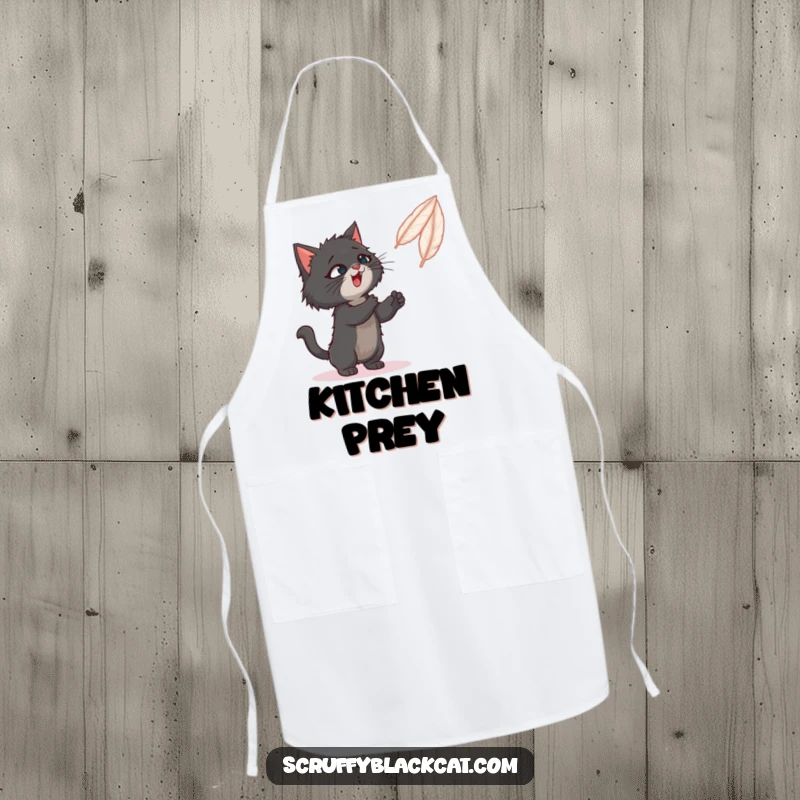 Funny apron showing a scruffy black cat playfully batting at a feather toy while someone cooks.