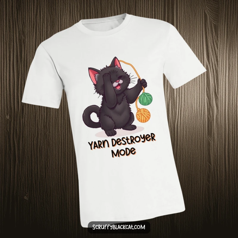 Funny t-shirt featuring a scruffy black cat intensely focused on batting a dangling yarn ball, capturing playful energy.