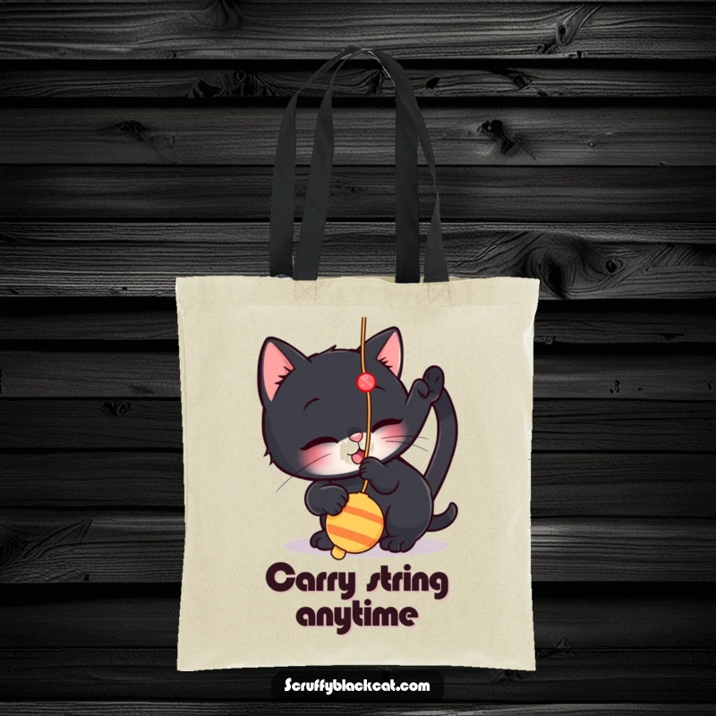 Funny tote bag showcasing a small black cat playfully batting at a dangling string toy, ideal for carrying items with a feline touch.